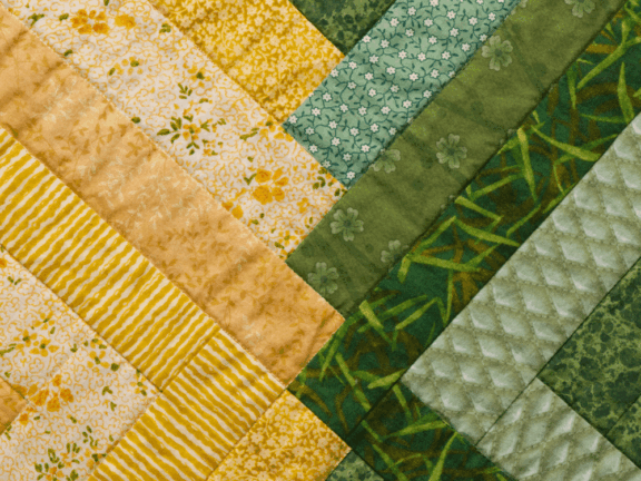 Close up of quilt composed of fabric strips in yellows and greens.